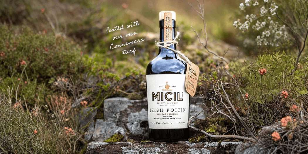 Micil Irish Poitín Heritage Edition bottle resting on mossy Connemara stone wall surrounded by wild heather and coastal vegetation, Galway Ireland