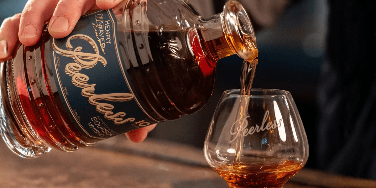 Peerless Henry Kraver's Old Reserve 10 Year Kentucky Bourbon being poured into a branded Peerless Glencairn glass on a barrel top