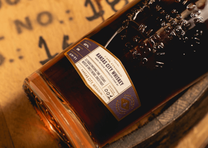 Close-up of J. Rieger & Co. Private Stock Kansas City Whiskey bottle label, showing barrel details and custom cask finish information on a wooden barrel background.