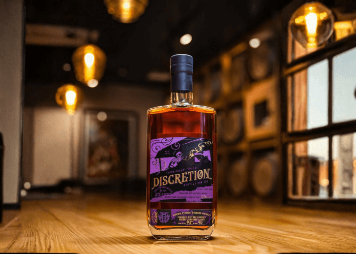 Bottle of Tarnished Truth Discretion PX Sherry Cask Finished Bourbon displayed in a warmly lit tasting room, with barrels in the background and soft evening light through the window.