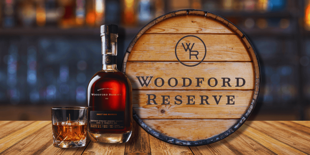Bottle of Woodford Reserve Sweet Oak Bourbon from the 2025 Master’s Collection next to a whiskey glass and a branded Woodford Reserve barrel on a wooden table.