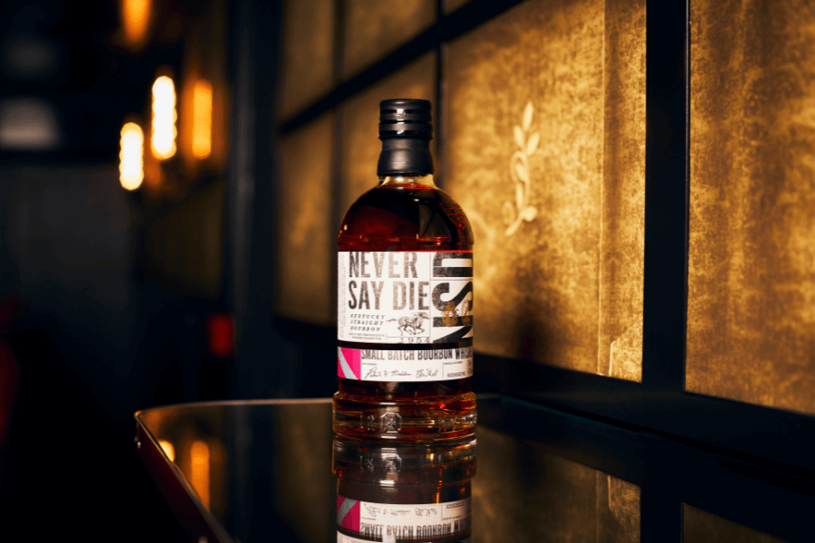 A bottle of Never Say Die Small Batch Bourbon sitting on a glass table